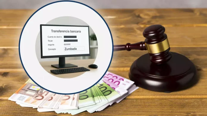 Pantalla de ordenador mostrando una transferencia con el concepto “Zumbada”, colocada sobre un fondo con un mazo de juez y dinero para ilustrar la condena a la empresa.