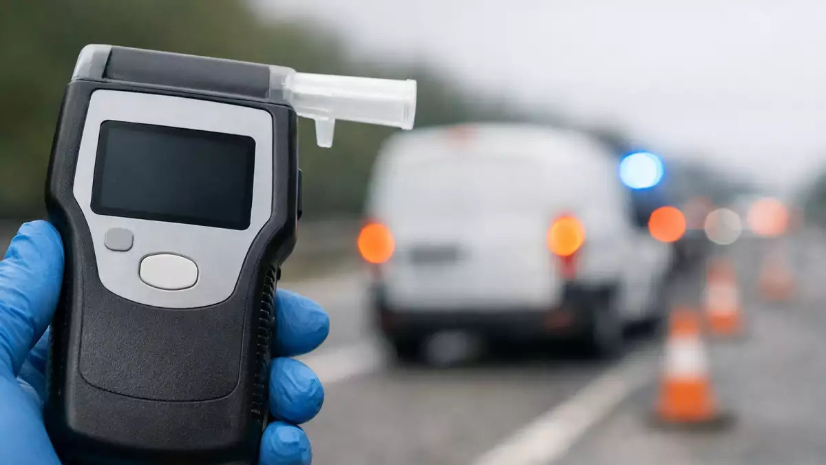 Alcoholímetro en primer plano durante un control en carretera, con una furgoneta de empresa detenida al fondo desenfocada