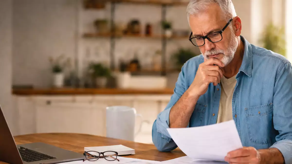 Trabajador de más de 60 años revisando documentos tras ser despedido y dudando si puede cobrar el paro antes de jubilarse