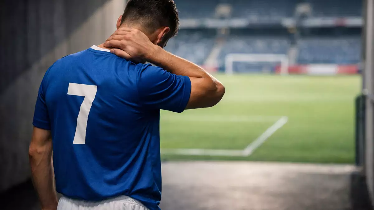 Futbolista de espaldas en el túnel de un estadio, con la mano en el cuello antes de salir al campo