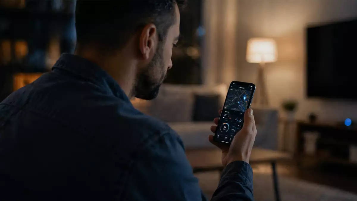 Man in a dark living room looking at a smartphone showing a map/navigation app on the screen.