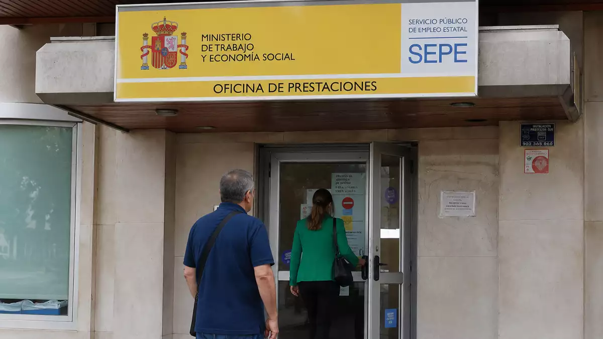 Entrance to a Spanish public employment service office (Oficina de Prestaciones) with SEPE sign above the door; two people approach the glass door.