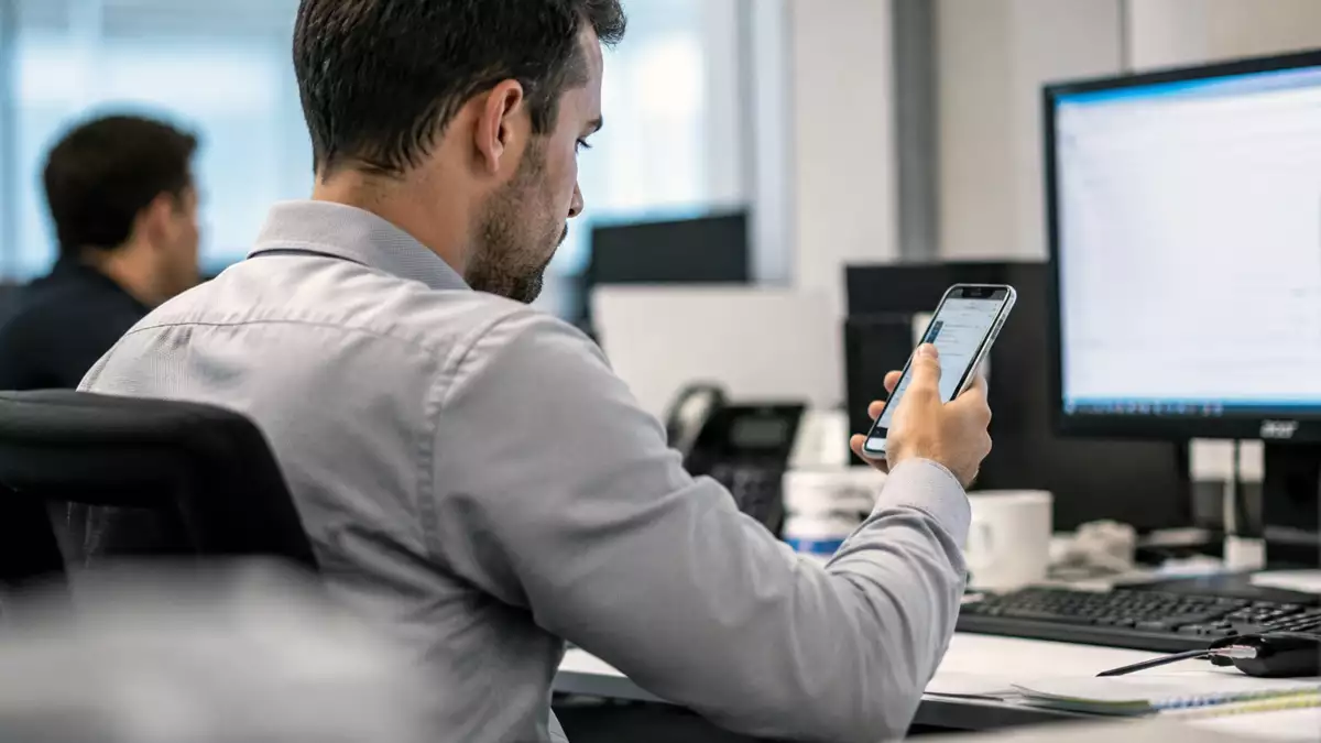 Trabajador utilizando un teléfono móvil durante su jornada laboral en una oficina.