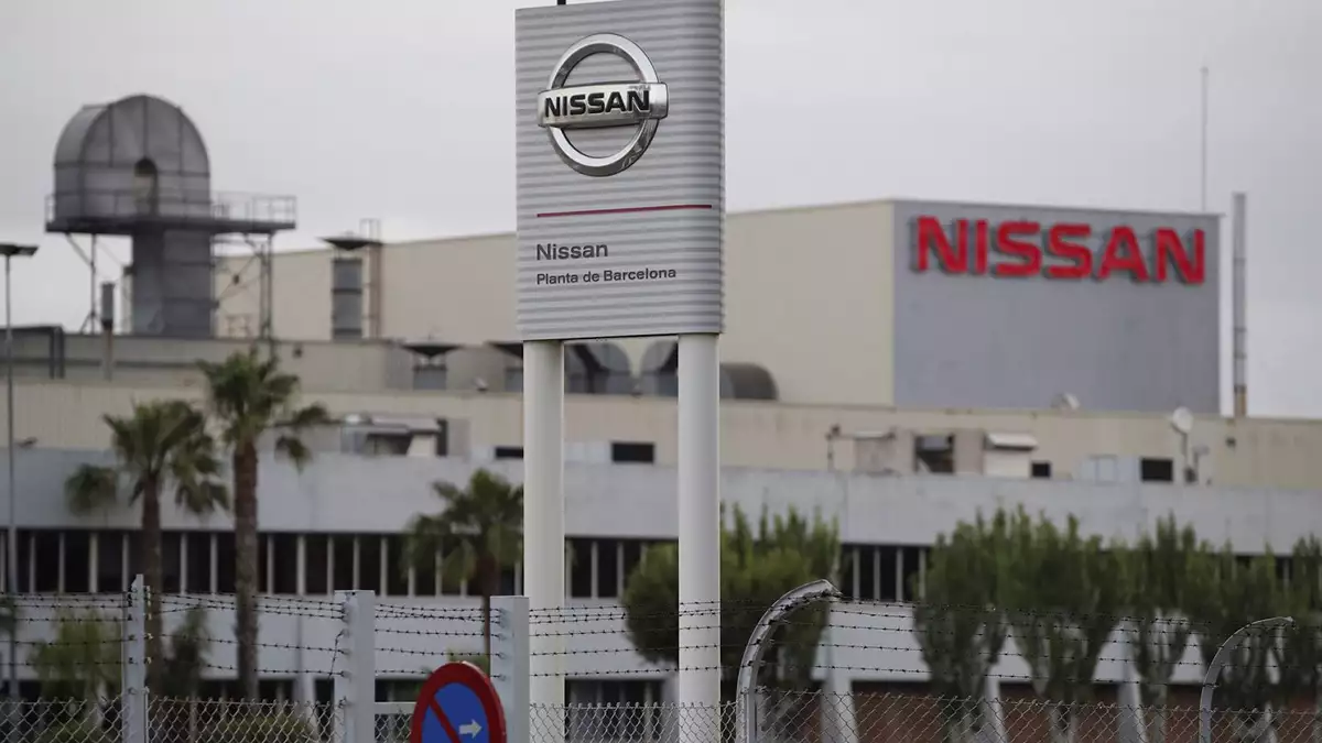 Nissan plant exterior with a tall sign reading 'Nissan' and 'Planta de Barcelona' in front of a factory building behind a barbed-wire fence.