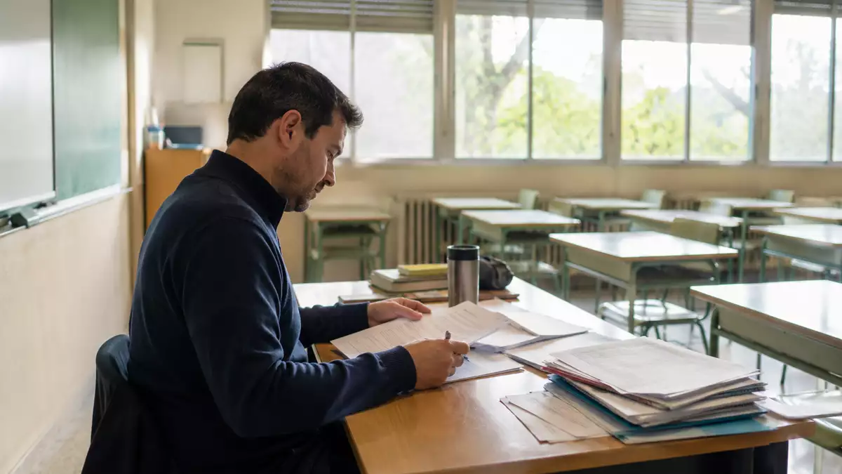 ALT Profesor interino en un aula vacía revisando documentación