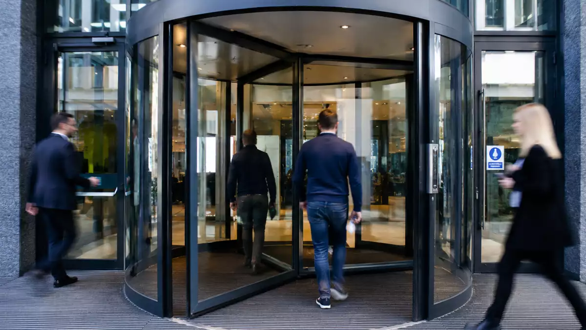Trabajadores entrando y saliendo por una puerta giratoria de oficinas, imagen que representa la rotación laboral en las empresas