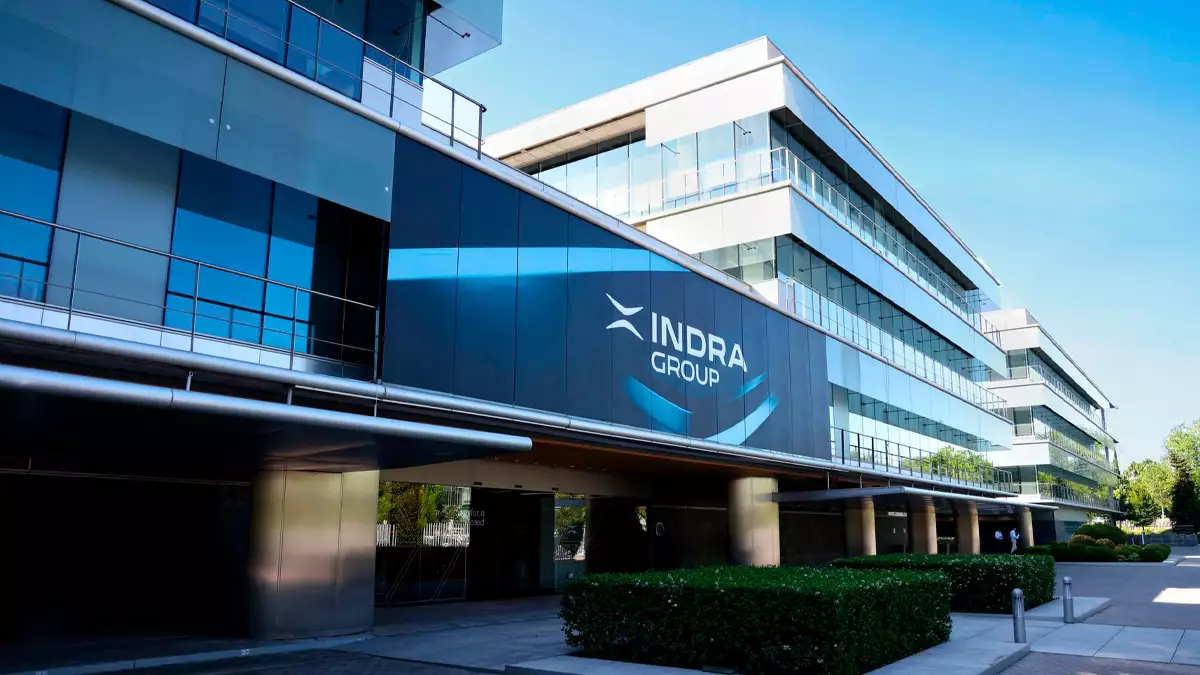 Modern office building with Indra Group signage along glass facade and blue sky after a sunny day, wide view.