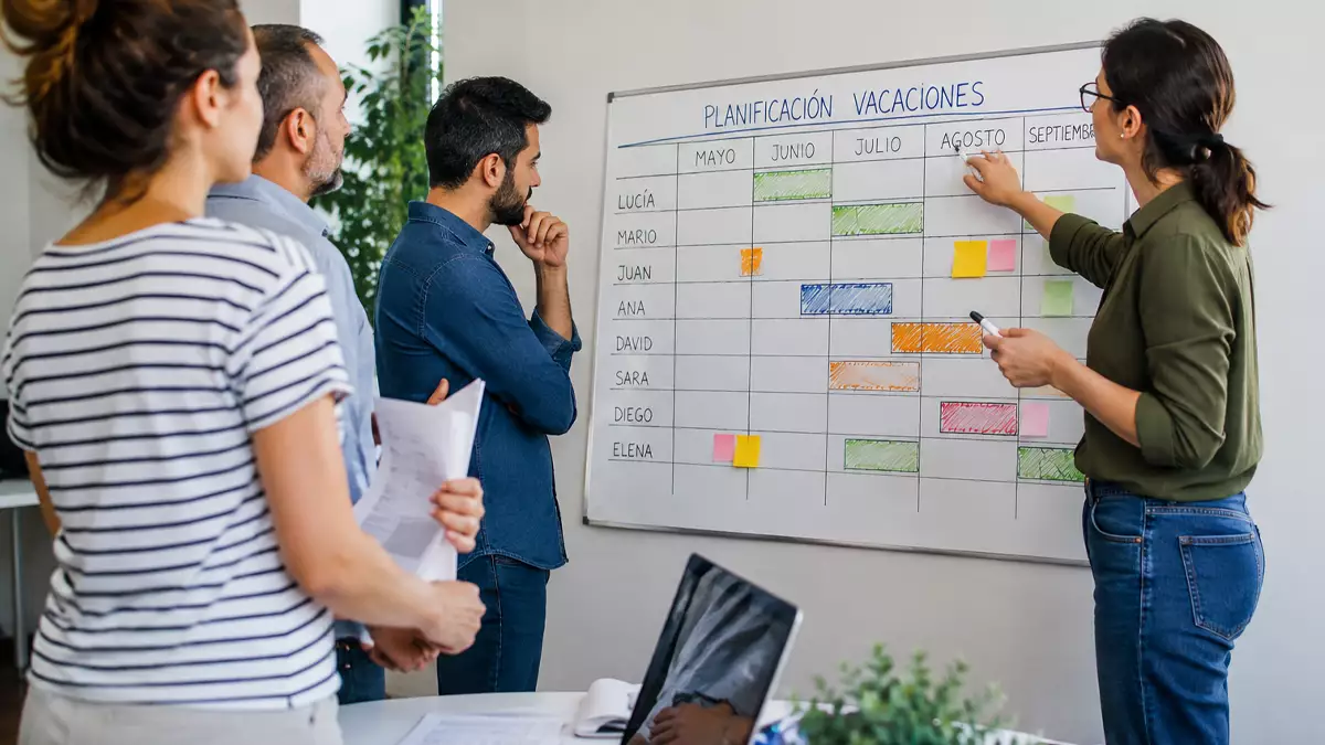 Trabajadores organizan el calendario de vacaciones de la empresa en una reunión de planificación. Imagen generada con inteligencia artificial.